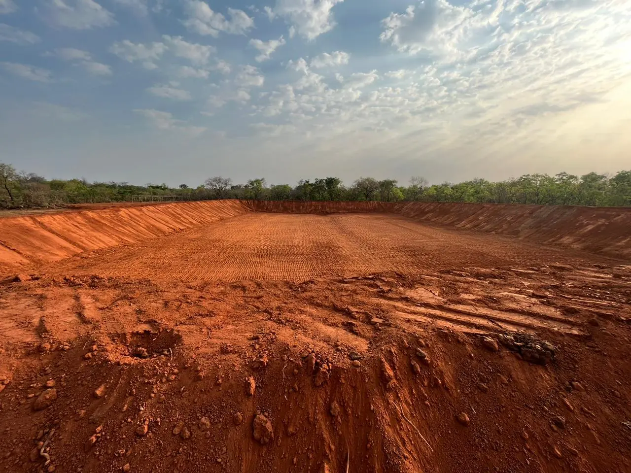 Freshly excavated pond with red earth walls at a processing site
