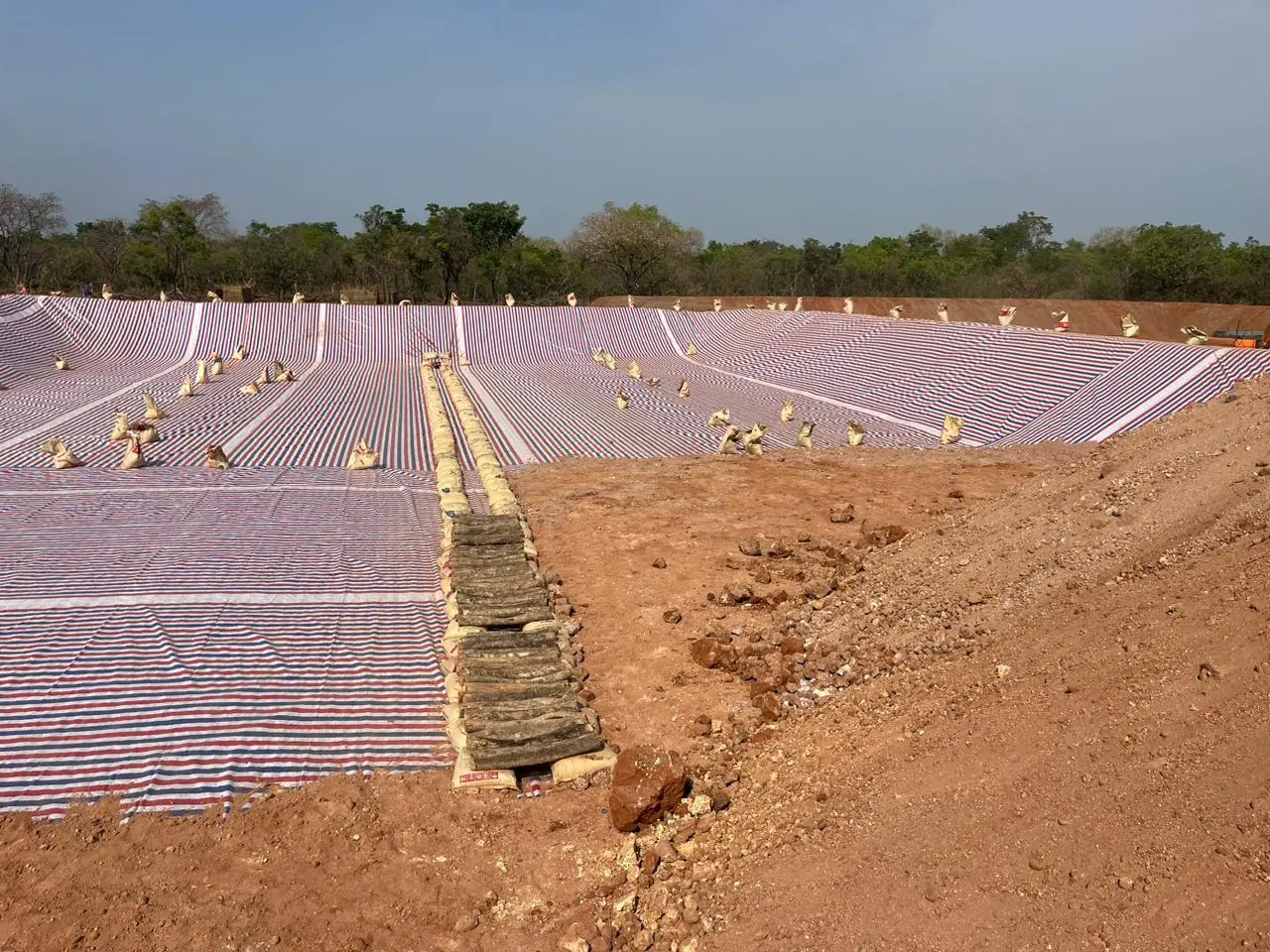Excavated pond covered with striped lining sheets held by sandbags