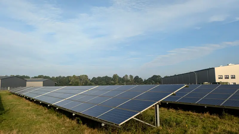Rows of ground-mounted solar panels beside industrial buildings
