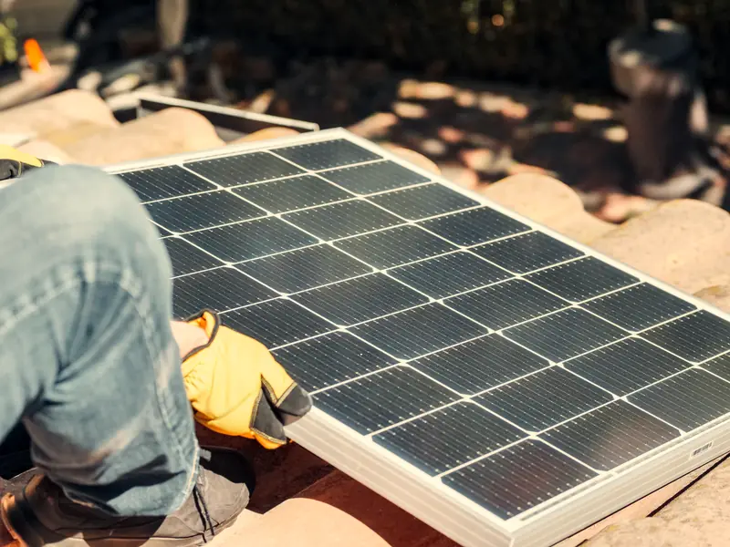 Installer in work gloves positioning a solar panel on a tiled roof