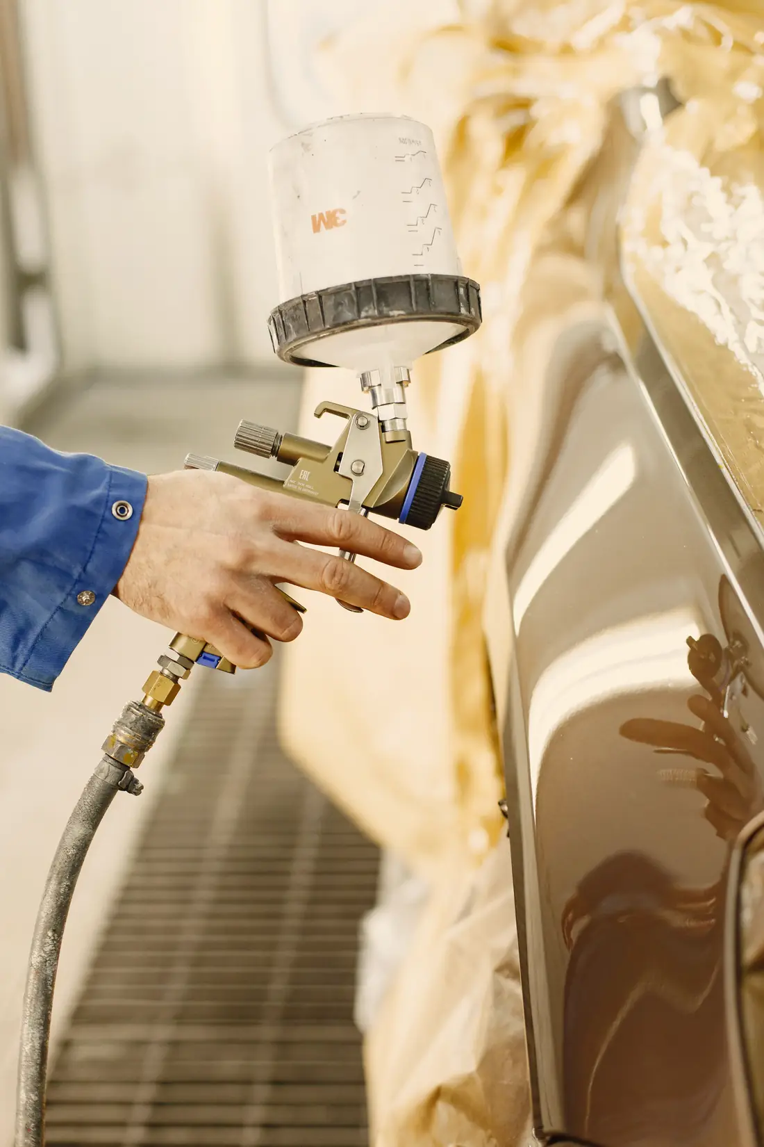 Painter's hand holding a spray gun beside a freshly painted car panel in a booth